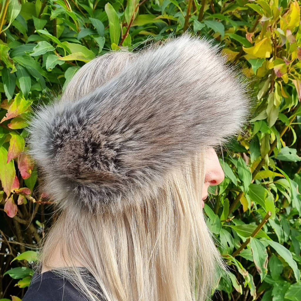 Person wearing a fur headband in shades of grey and brown with a green leafy background