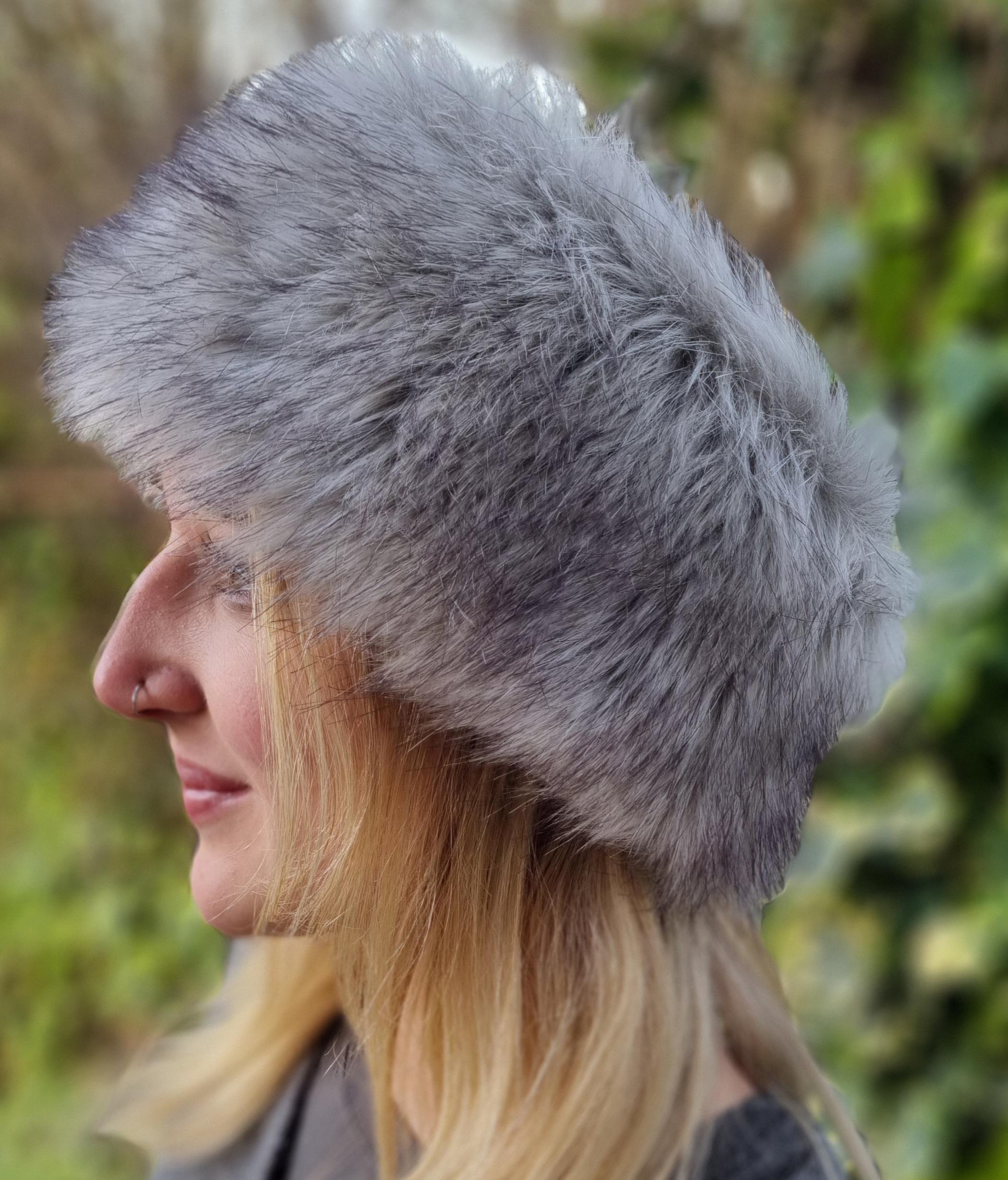 Person wearing a gray fur hat with a blurred natural background