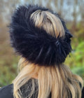 Black faux fur hat worn by a person with blonde hair, against a blurred natural background.