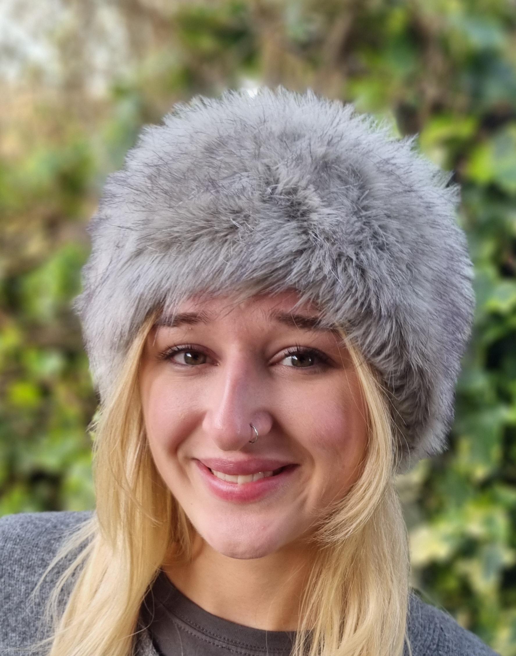 Person wearing a gray fur hat with a blurred green background