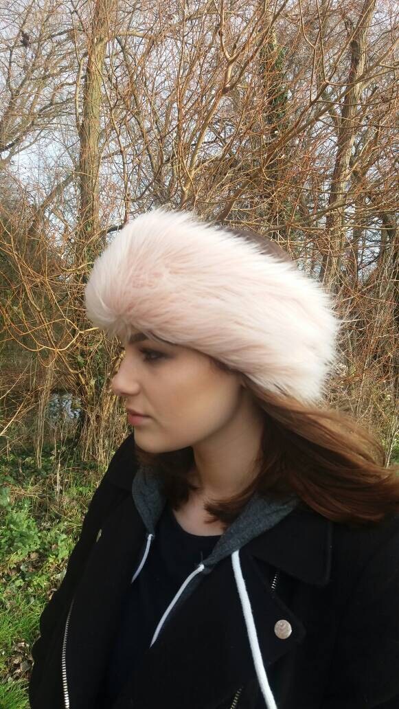 Woman wearing a light pink fur headband outdoors with bare trees in the background