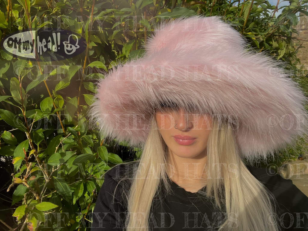 Person wearing a large pink fur hat with a blurred background Pamela Anderson style hat