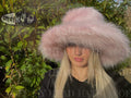 Person wearing a large pink fur hat with a blurred background Pamela Anderson style hat