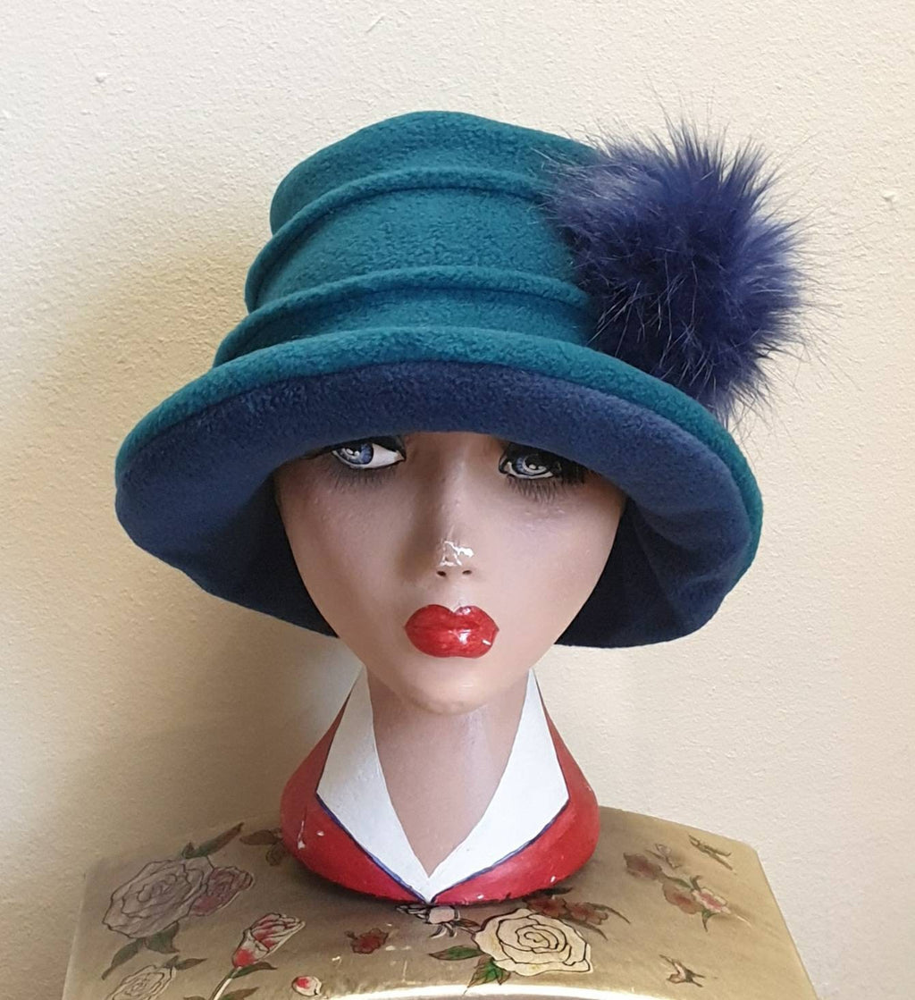 Teal green fleece cloche hat with faux fur pom pom finish, worn on a mannequin head, handmade in England