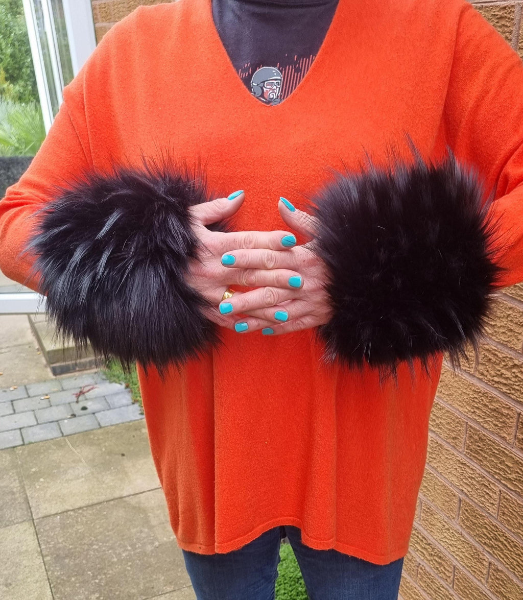 Person wearing an orange sweater with black fluffy arm cuffs, standing outdoors.