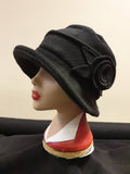 Black cloche hat with a flower detail on a mannequin head against a beige background