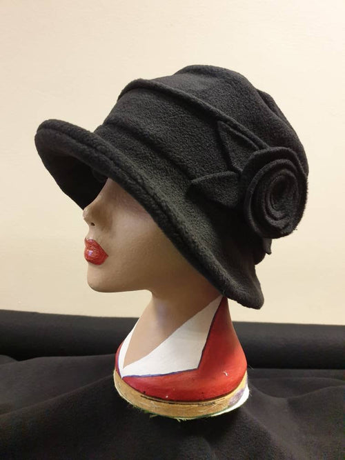 Black cloche hat with a flower detail on a mannequin head against a beige background