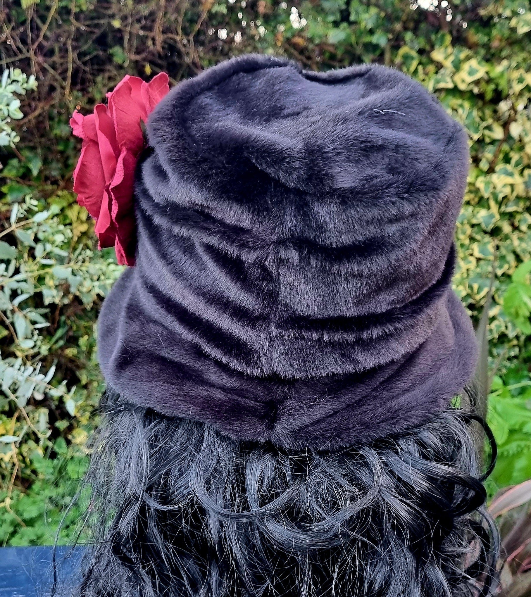 black fur hat with a red flower against a green leafy background