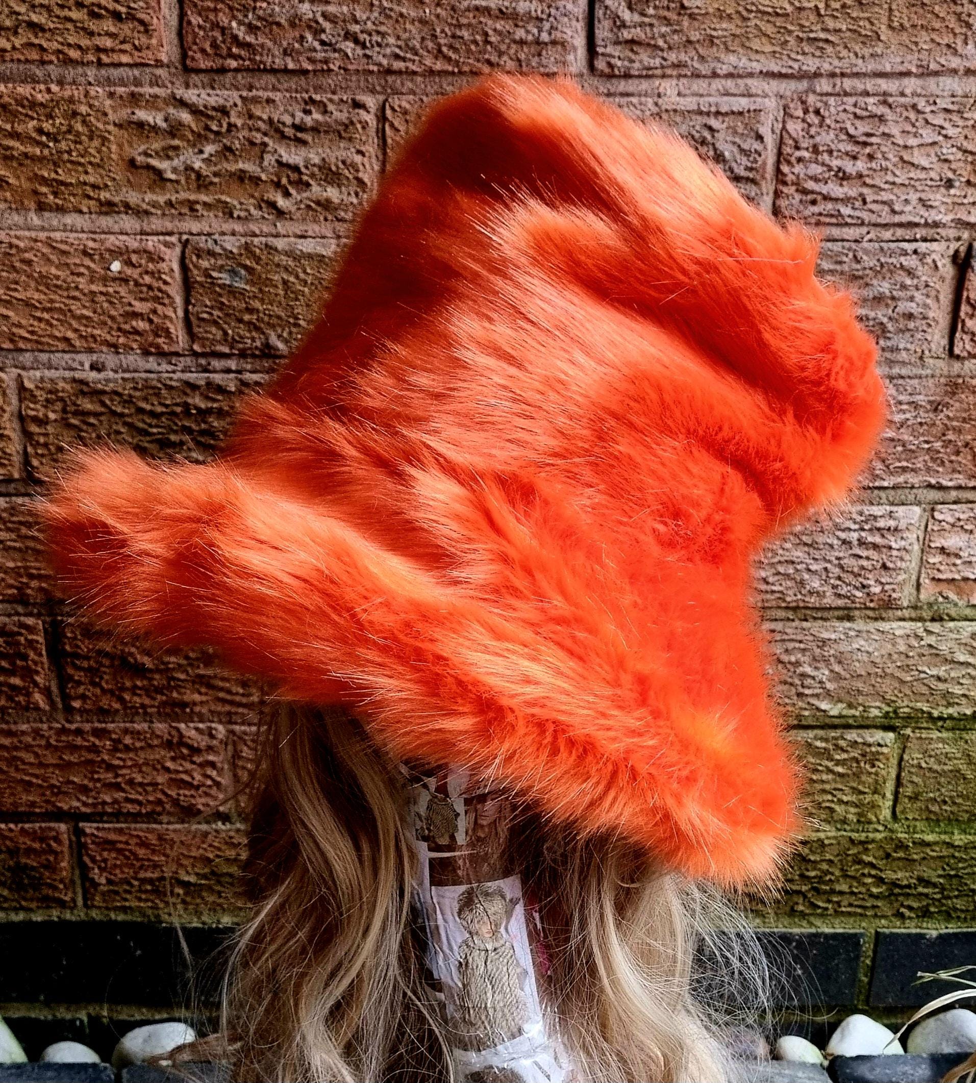 Side view of oversized orange faux fur hat showing sculptural tall crown