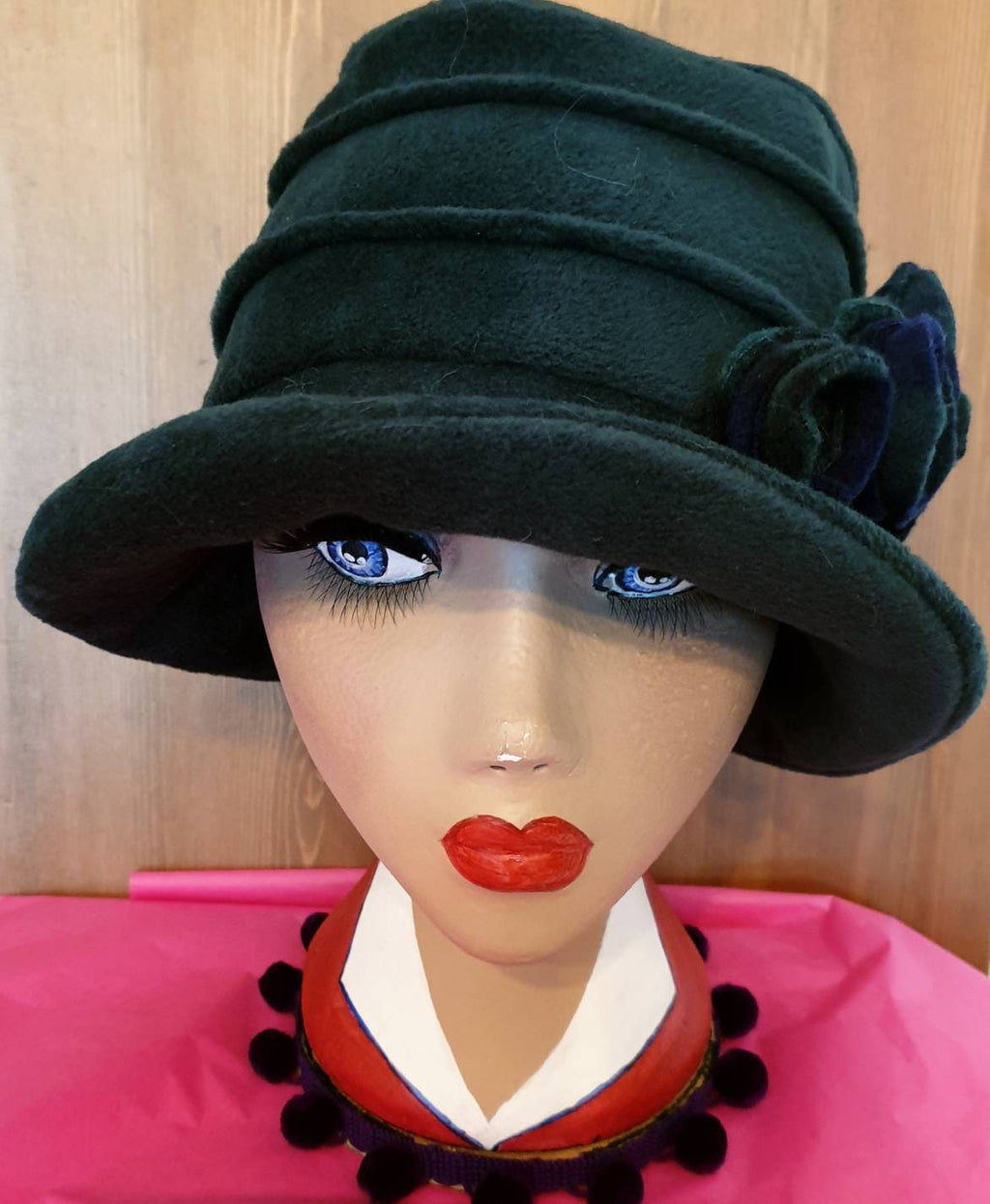 Mannequin head wearing a dark green hat with a wooden panel background