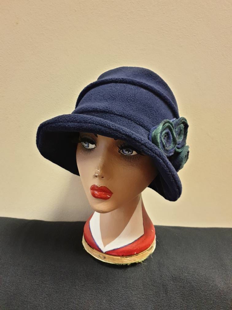 Navy blue cloche hat with a green flower on a mannequin head against a beige background