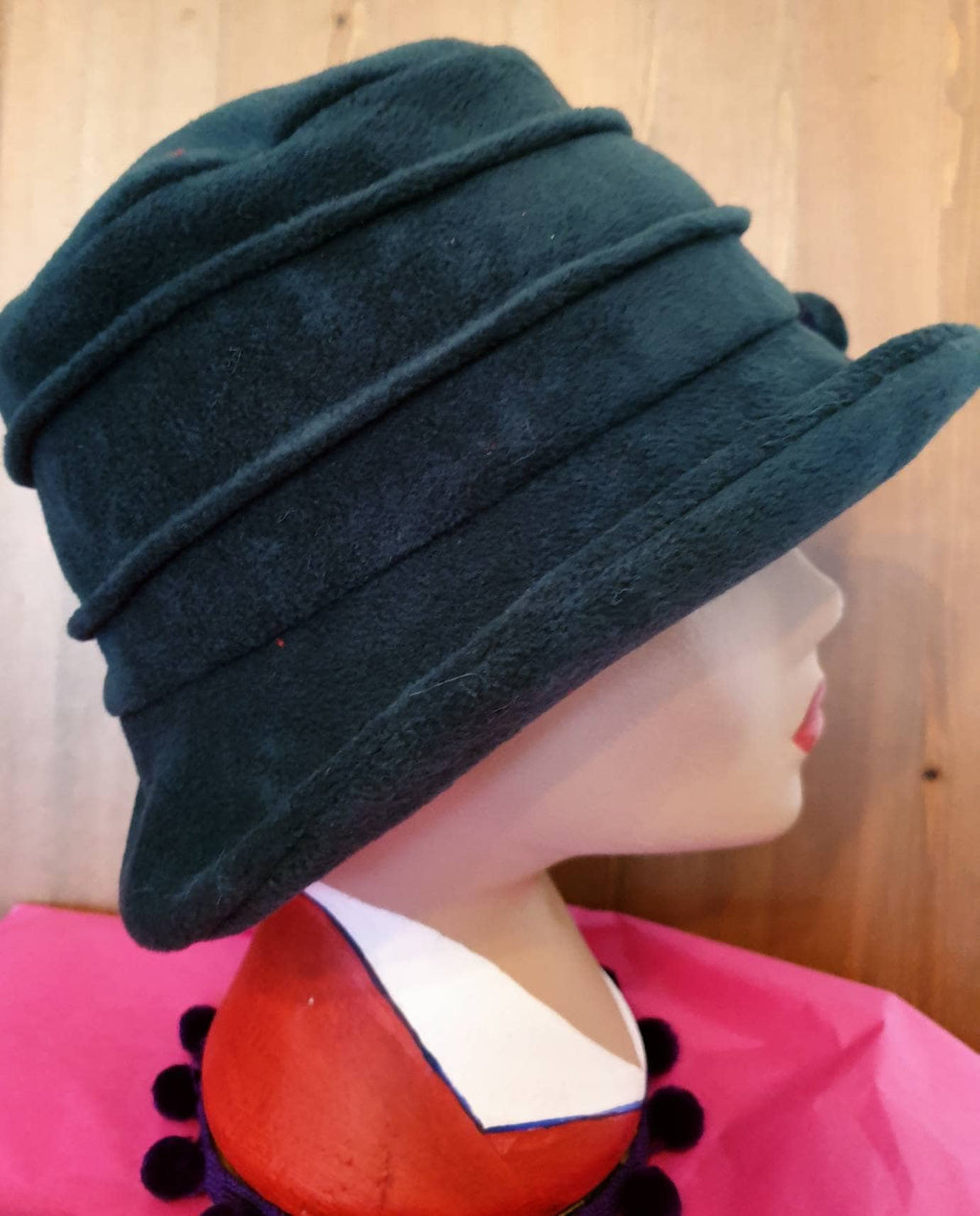 Dark green hat on a mannequin with a colorful dress against a wooden background