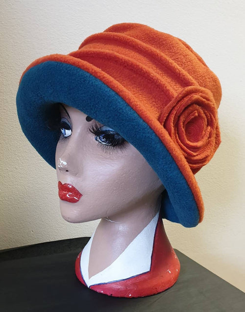 Handmade fleece cloche hat in burnt orange and teal, with spiral rosette detail — made to order in Nottingham, UK