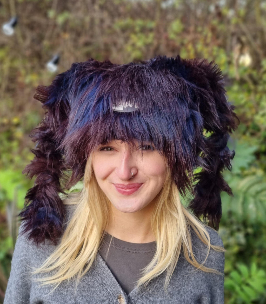 Person wearing a unique, dark-colored hat with pigtails against a blurred natural background