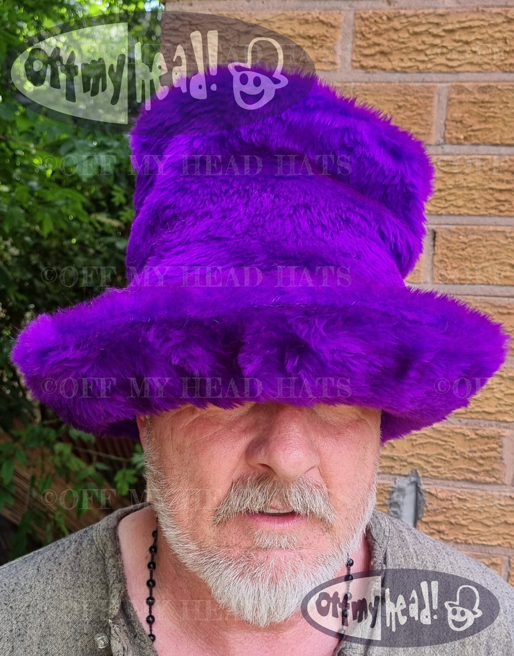 Man wearing a purple fur hat with 'Off My Head Hats' branding against a brick wall.