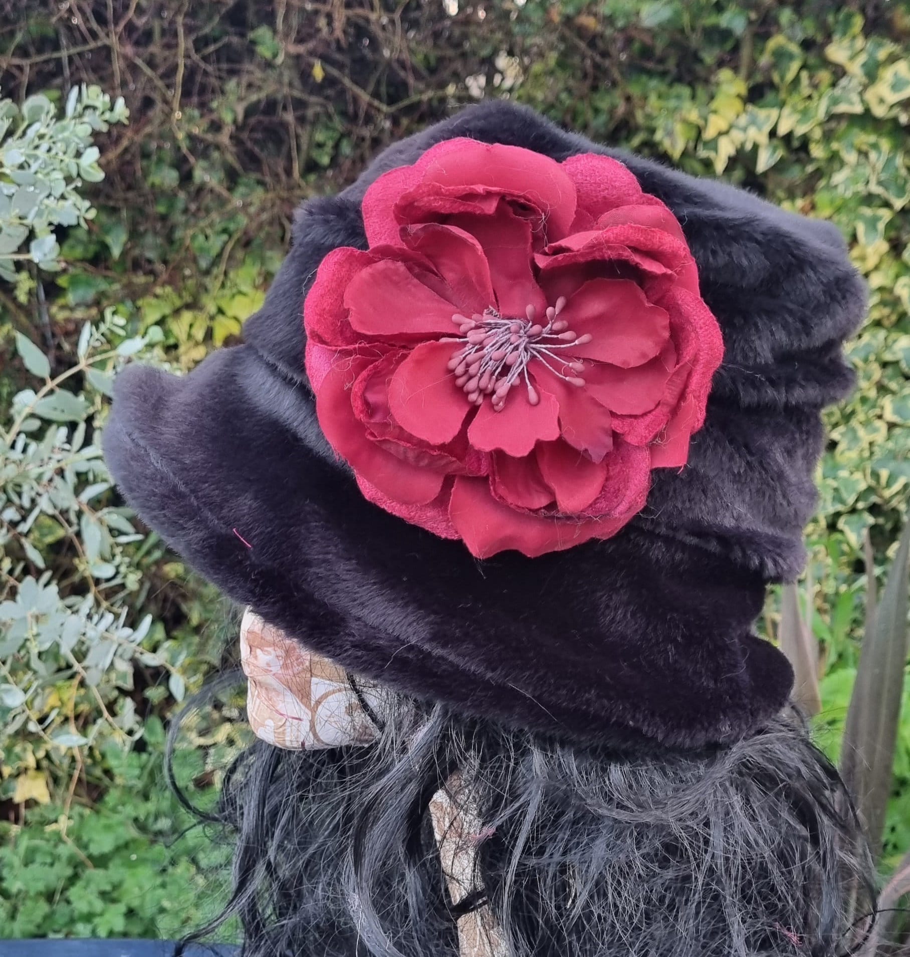Black fur hat with a large red flower on a mannequin against a natural background