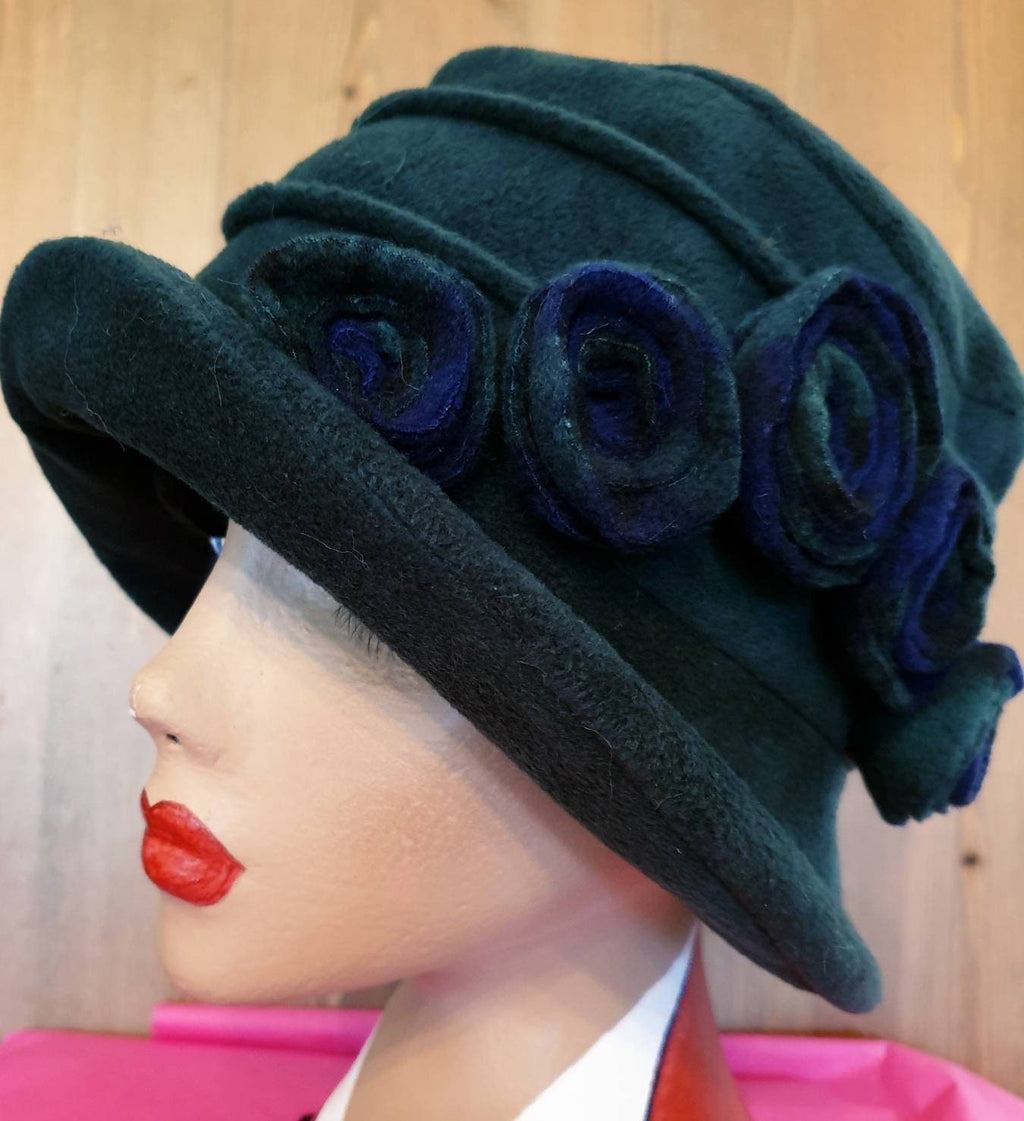 Dark green cloche hat with blue flowers on a mannequin head against a wooden background