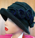Dark green cloche hat with blue flowers on a mannequin head against a wooden background