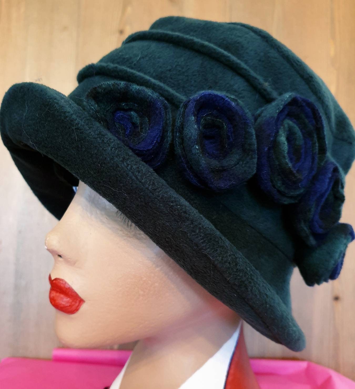 Dark green cloche hat with blue flowers on a mannequin head against a wooden background