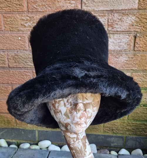 Black fur hat on a mannequin head against a brick wall.
