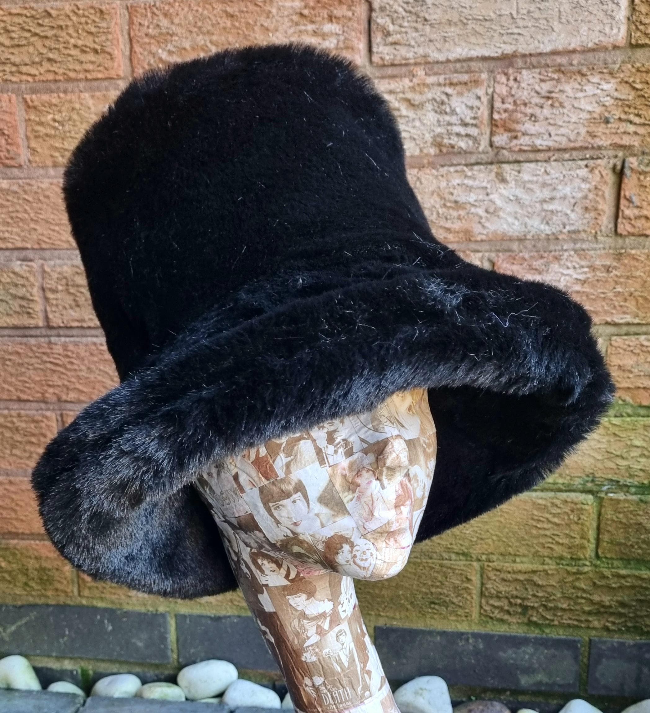 Black fur-trimmed hat on a mannequin head against a brick wall.