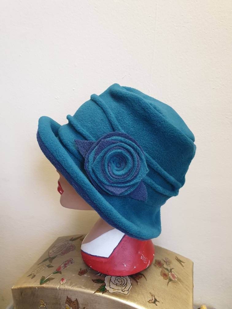 Teal green fleece cloche hat with large two-tone flower trim, worn on a mannequin head, handmade in England