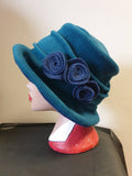 Teal green fleece cloche hat with three airforce blue flowers, worn on a mannequin head, handmade in England