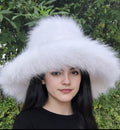 Person wearing a large white fur hat with a green leafy background