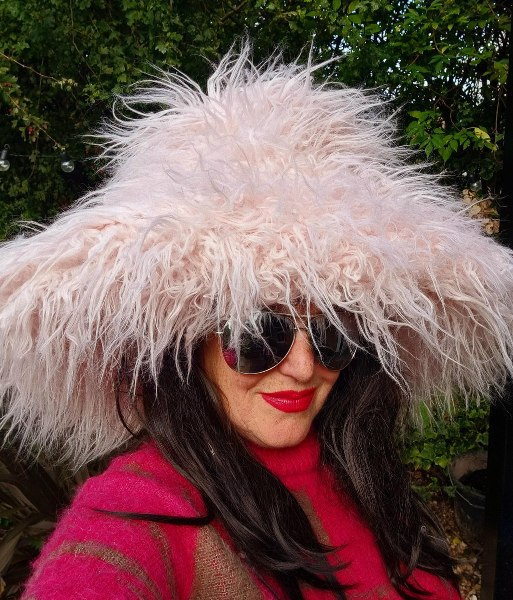 Person wearing a fluffy pink hooded coat with sunglasses and red lipstick outdoors.